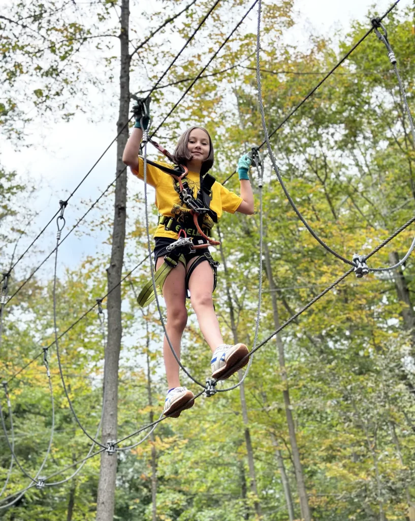 Girl traversing aerial obstacle in the tree tops.